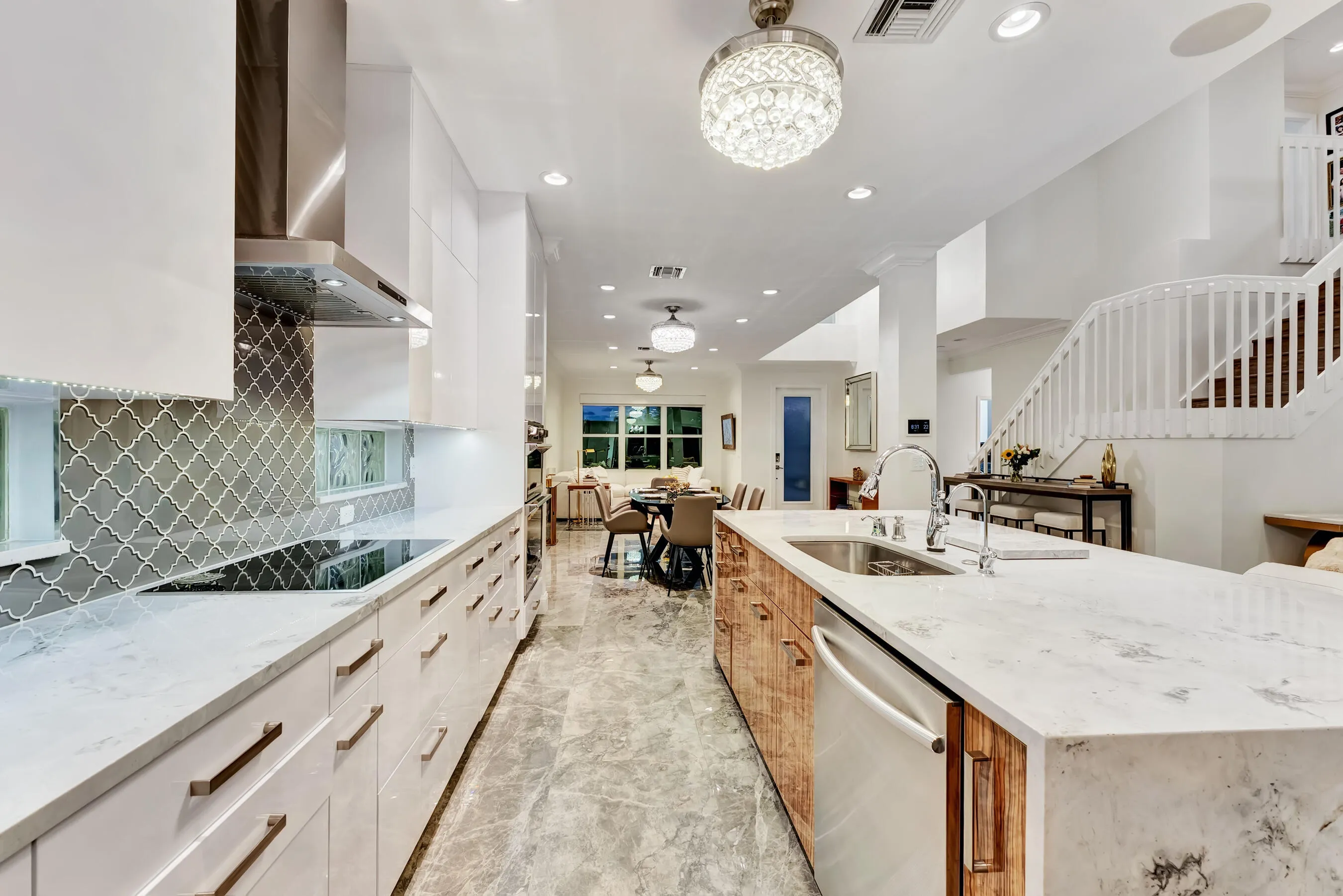 Evening view down the full kitchen with staircase and lit backsplash visible beyond.