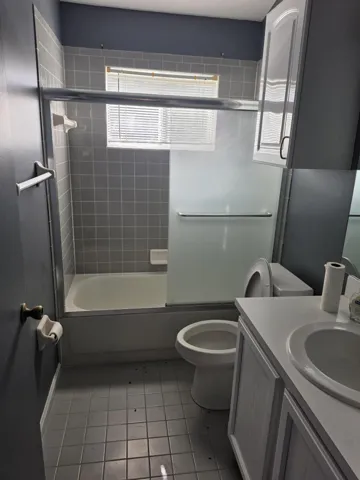Bathroom featuring a tiled shower enclosure with a clear glass panel, a white vanity with an integrated sink, and a commode
