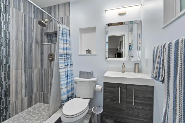 Bathroom featuring a walk-in shower with vertical tile and mosaic accent, a wall-mounted vanity with integrated sink, a mirrored medicine cabinet, and built-in shelving