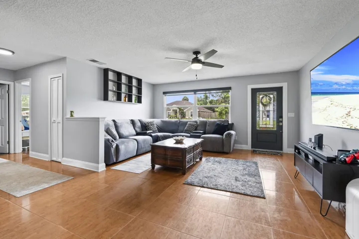 Spacious living area featuring neutral wall tones, tile flooring, a ceiling fan, and a front entry door with decorative glass inserts