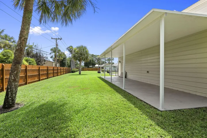 Expansive rear lawn featuring mature palm trees and a wooden privacy fence