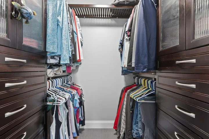 Custom walk-in closet featuring built-in dark wood cabinetry, multiple drawers, glass-front upper cabinets, and extensive hanging rods