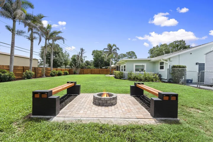 Expansive green lawn with a paver patio and circular stone fire pit, privacy fence and lush landscaping