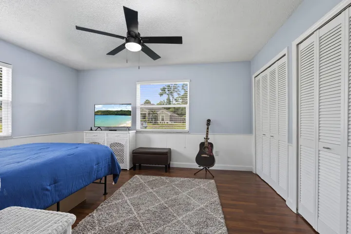 Spacious room featuring wood-finish flooring, two windows with blinds, a ceiling fan with integrated lighting, and two sets of louvered bifold closet doors