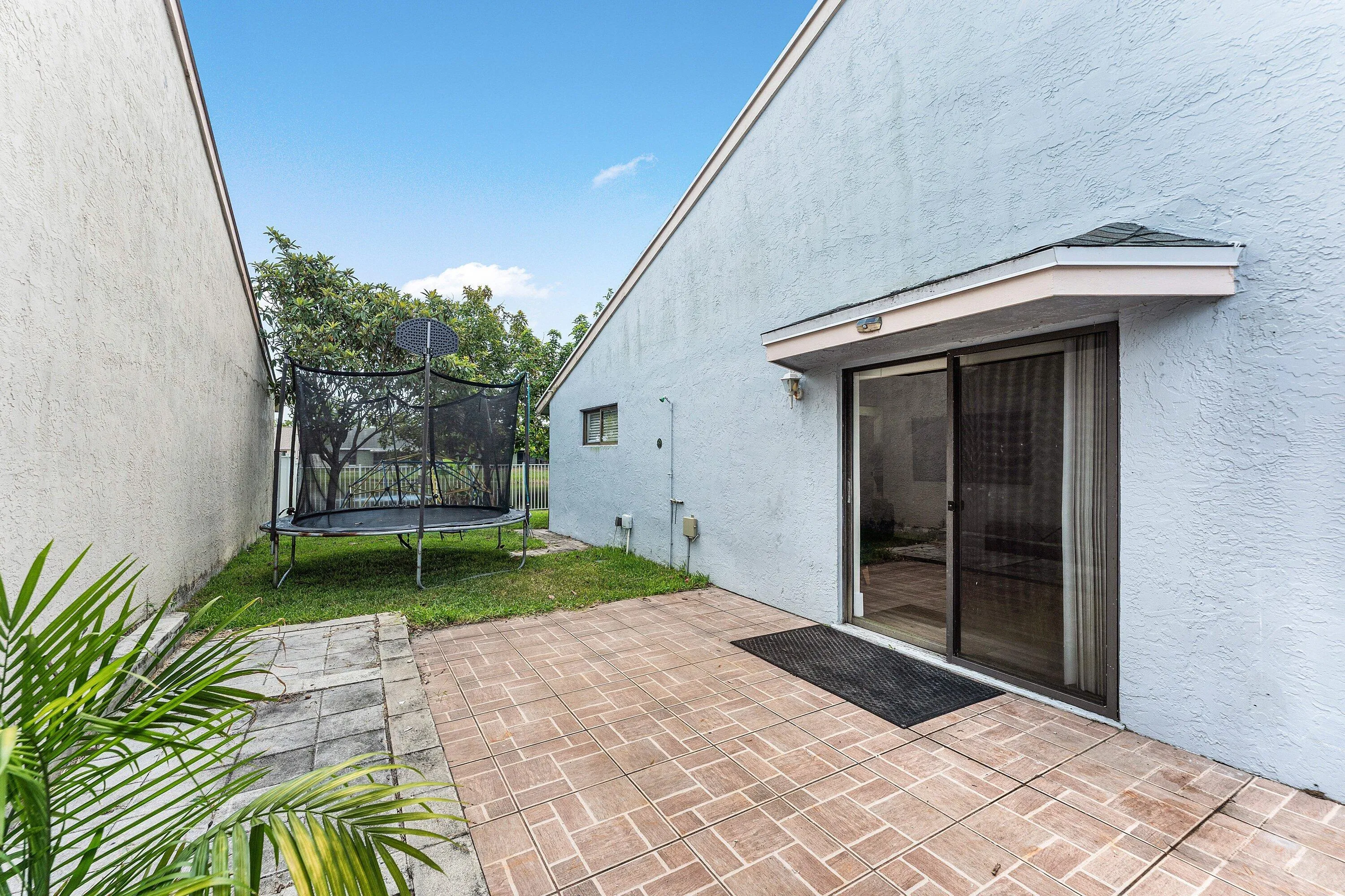 Exterior patio featuring brick-patterned pavers and a sliding glass door entry with an overhang