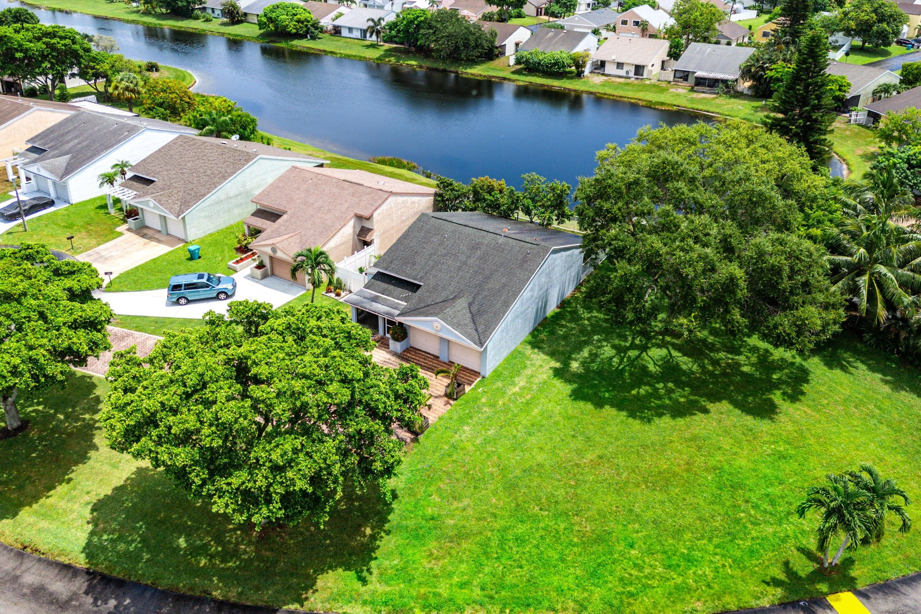 Waterfront property featuring a lush green lawn, mature trees, and a paved driveway