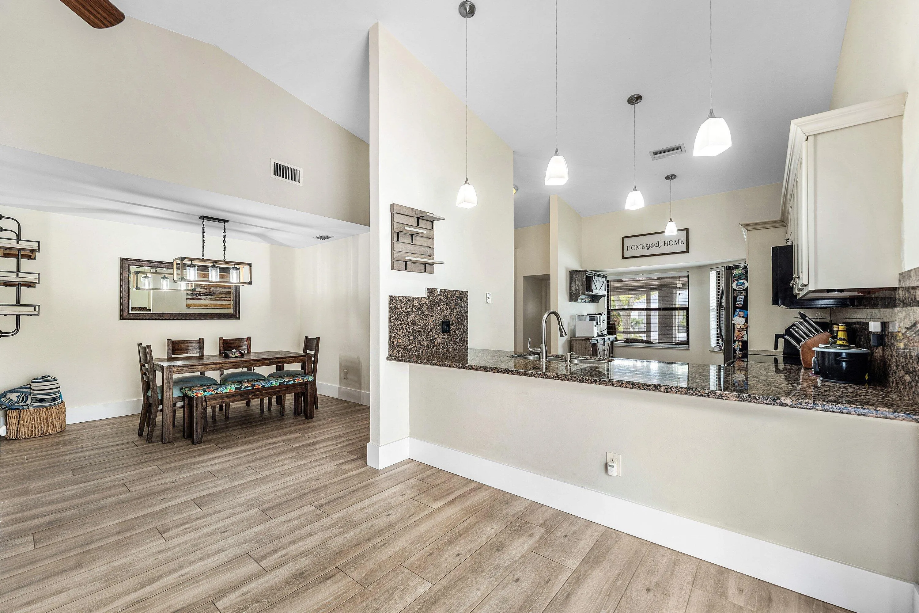 Open-concept kitchen and dining area featuring wood-finish flooring, vaulted ceilings, and a breakfast bar with granite countertops