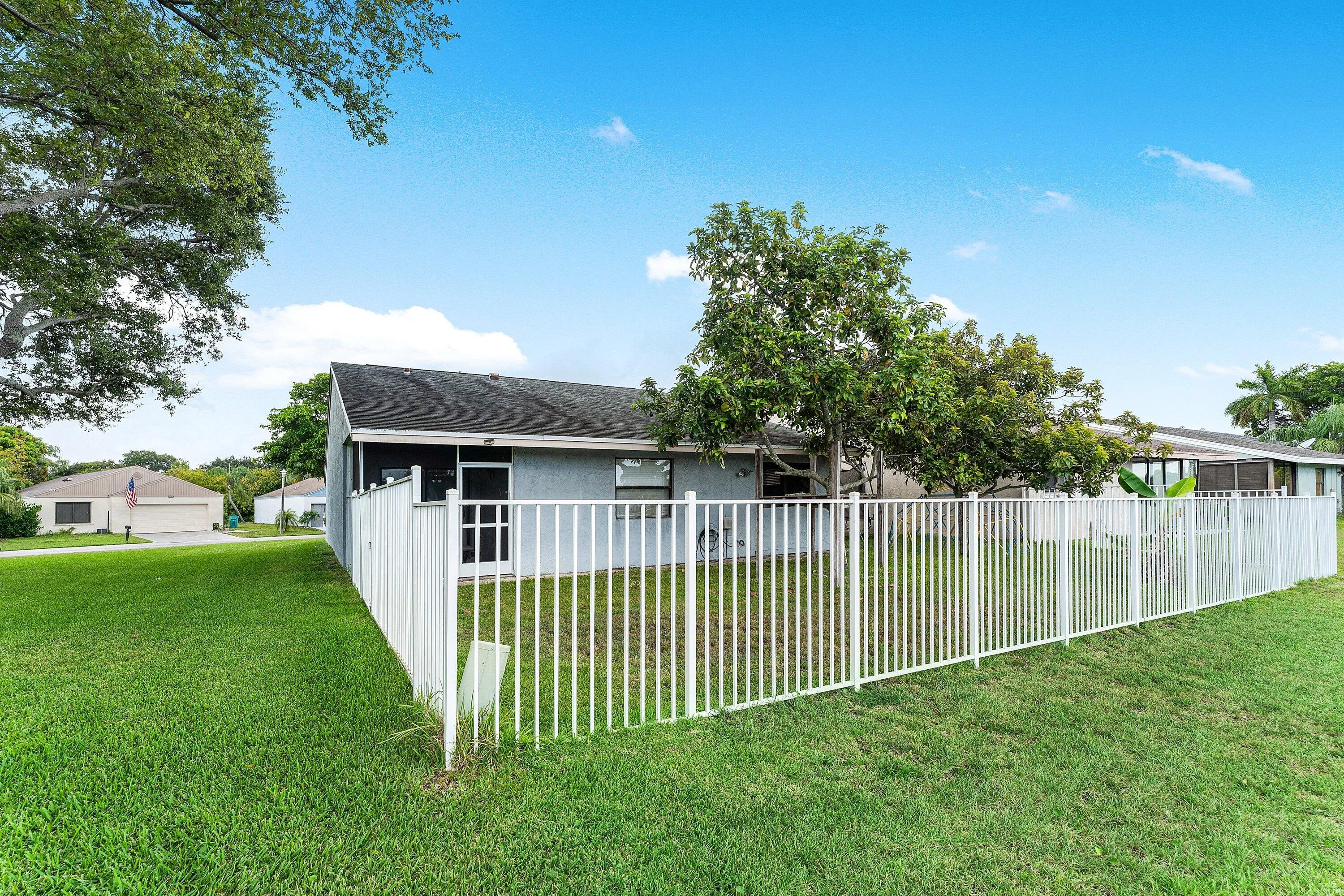 Expansive green lawn bordering a white picket fence, surrounding a residence with a gray exterior and dark roof