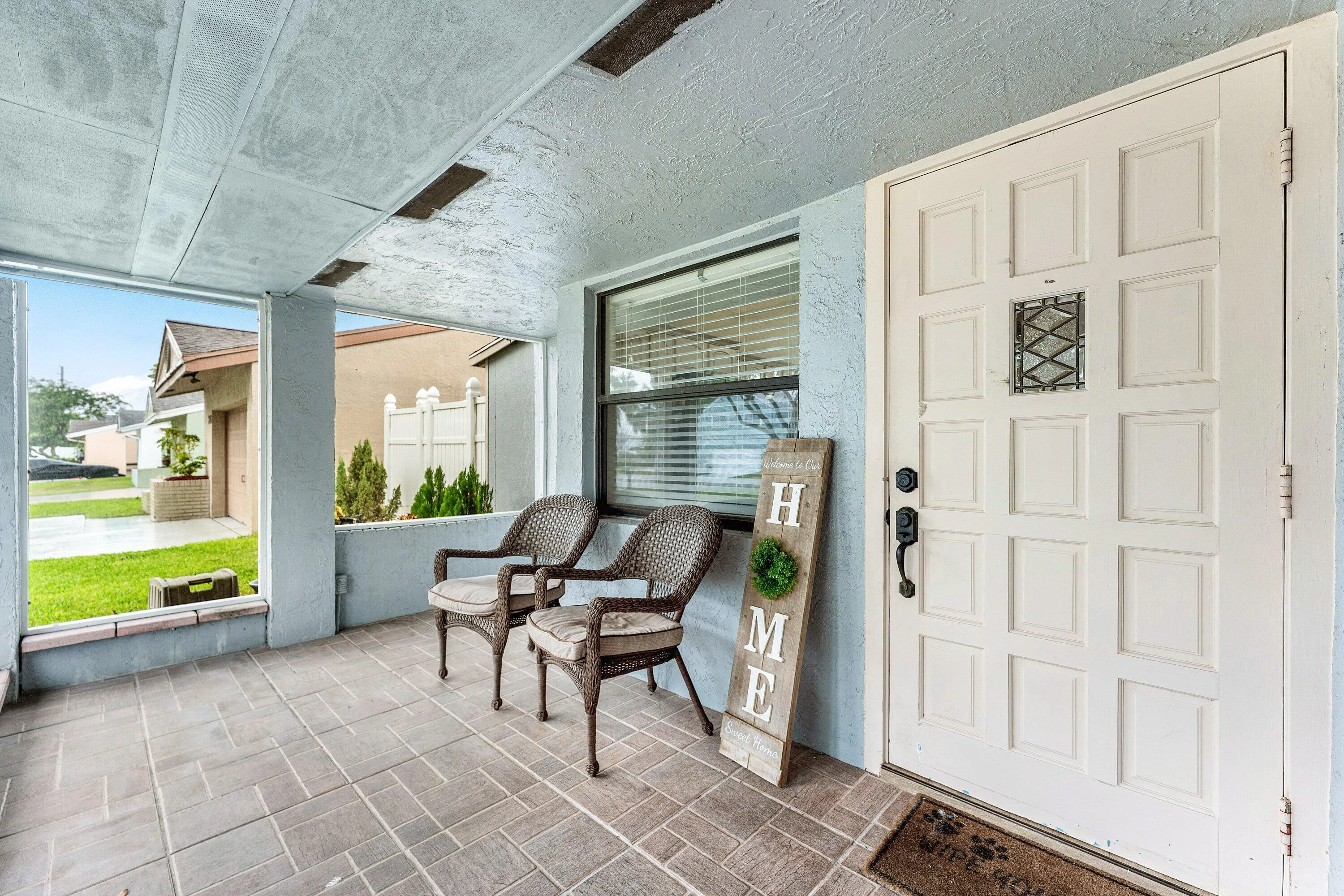 Covered front porch featuring a paneled entry door with decorative ironwork, tile flooring, and a large window with blinds