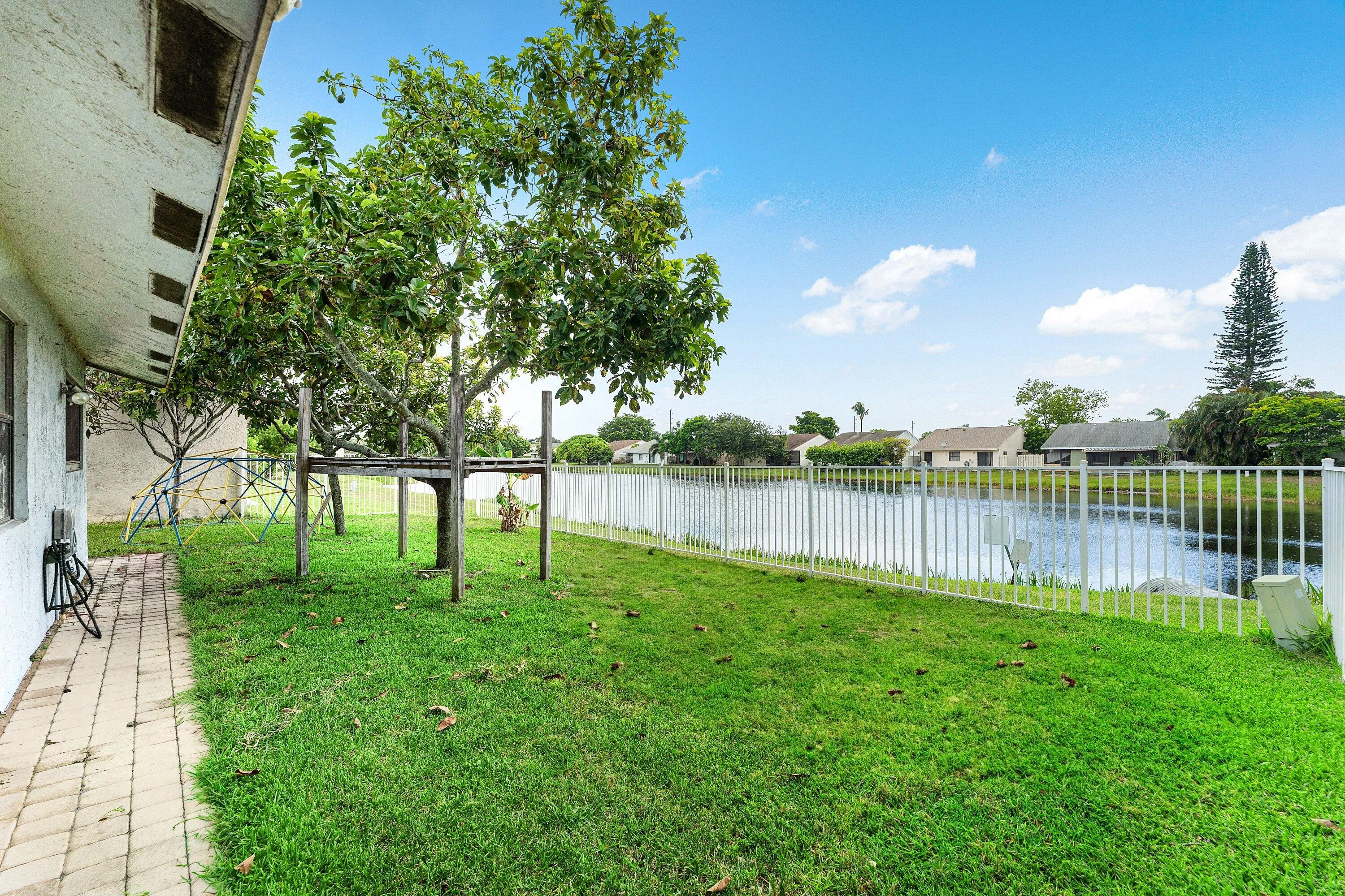 Expansive green lawn backing onto a pond, secured by a white perimeter fence