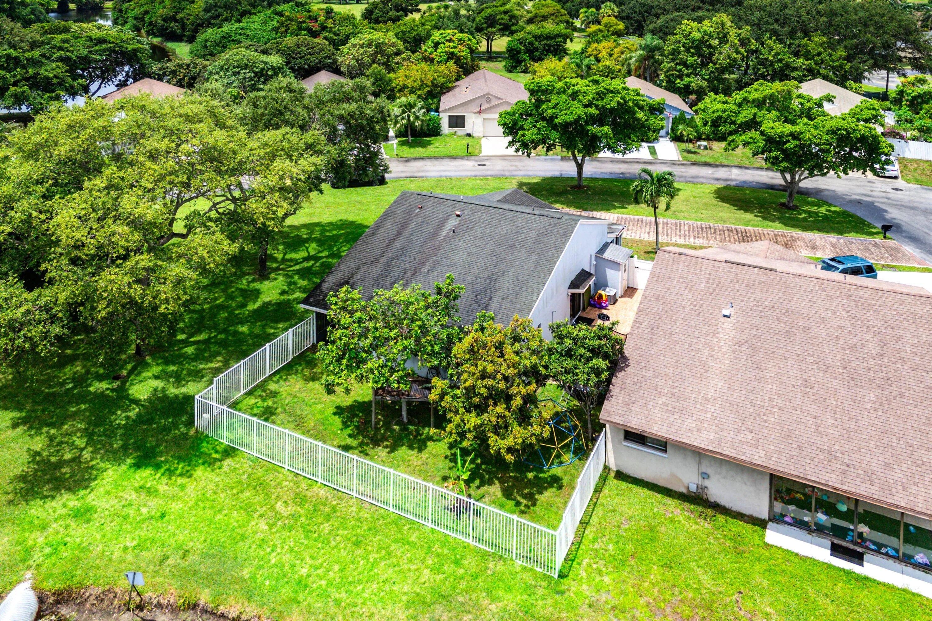 Expansive green lawn with mature trees, featuring a white fence enclosing a portion of the property