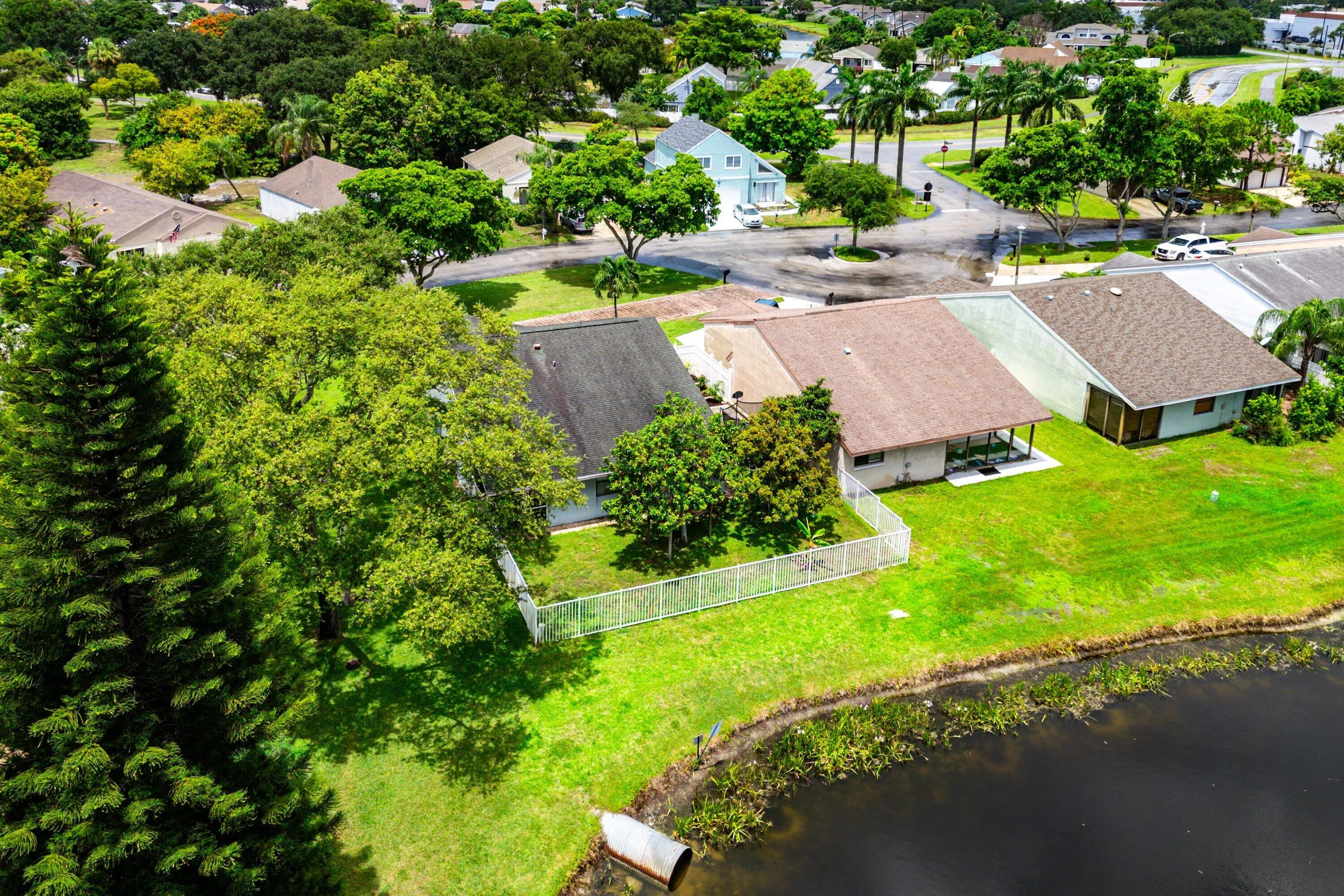 Waterfront property featuring a private fence, lush green lawn, mature trees, and a paved street