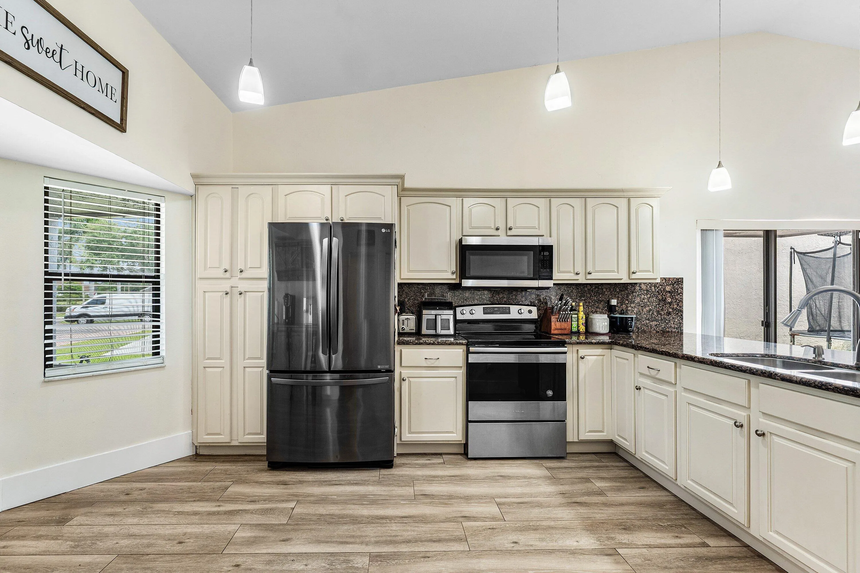 Kitchen featuring light-toned cabinetry, dark patterned countertops, stainless steel appliances, and wood-finish flooring