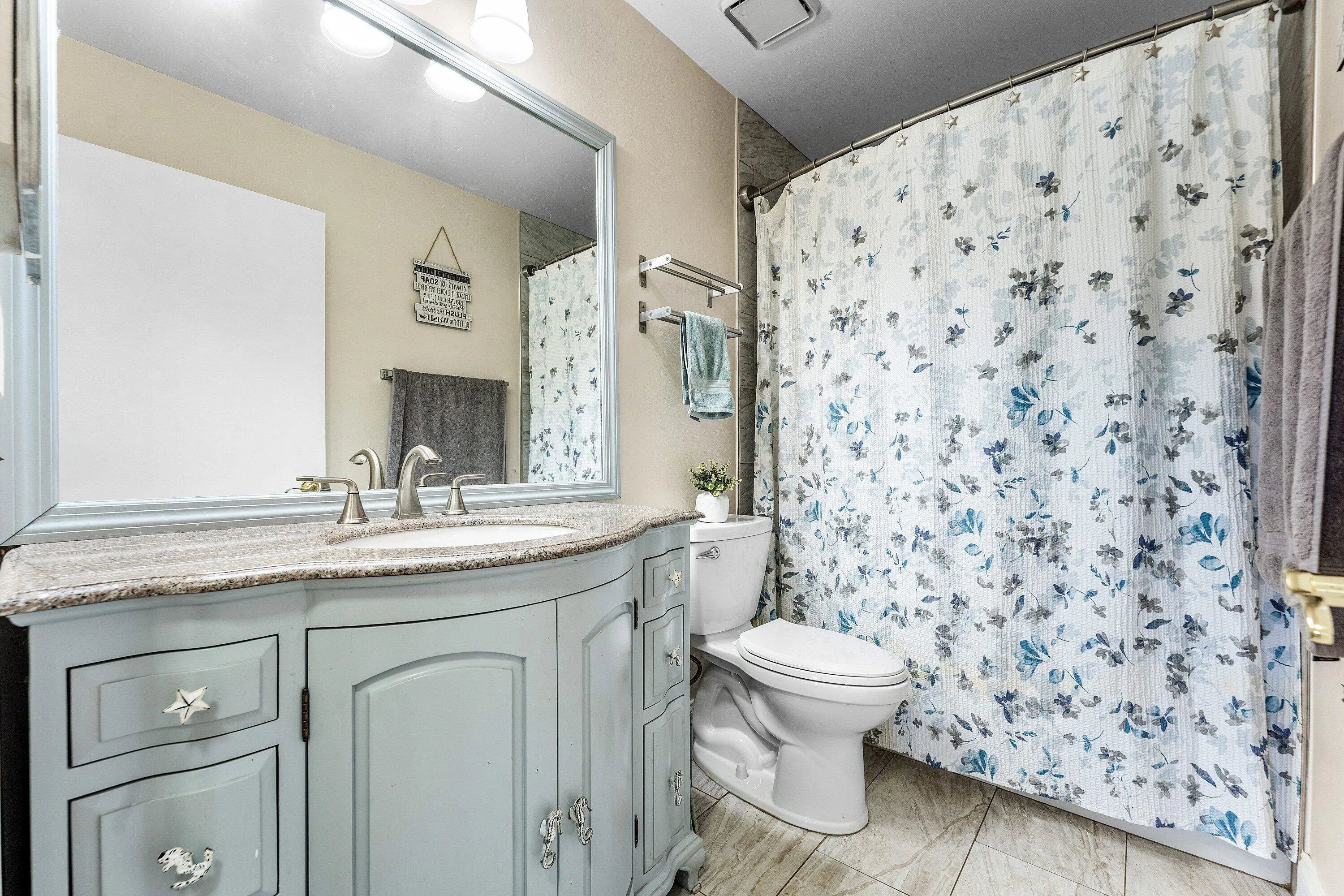 Bathroom featuring a light blue vanity with a curved front, a granite-look countertop, and a vanity mirror with overhead lighting