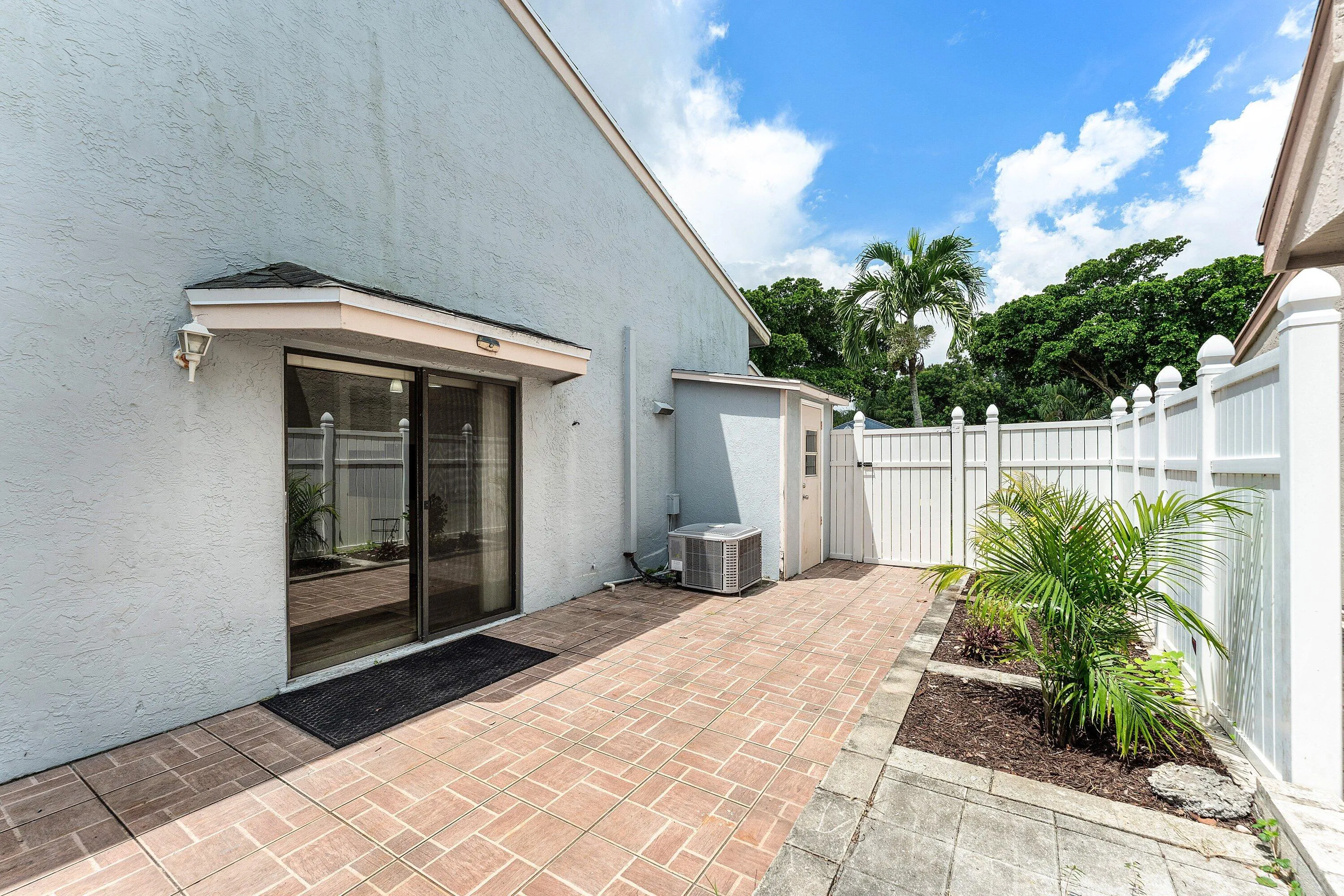 Private outdoor patio featuring brick paver flooring, white privacy fencing, and tropical landscaping