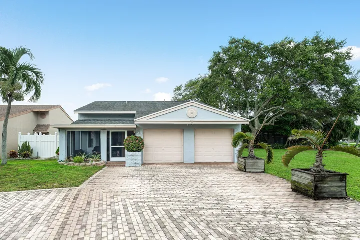 Light blue exterior with a two-car garage, screened-in porch, and a patterned paver driveway