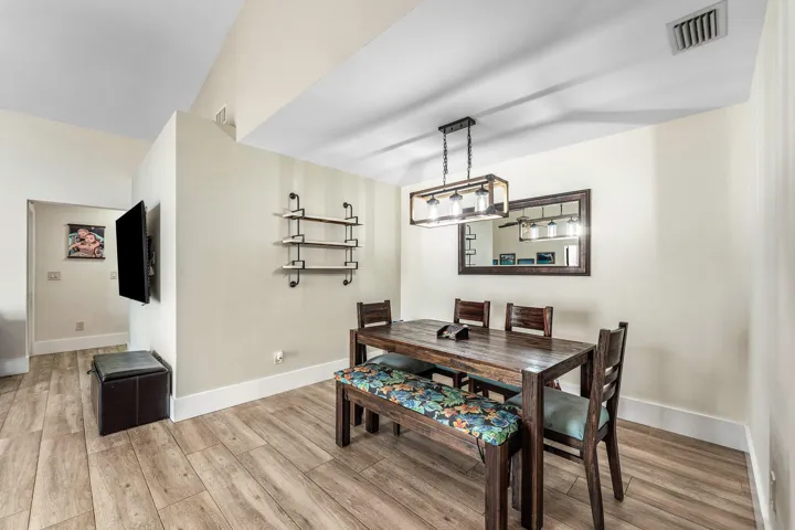 Wood-finish flooring extends throughout this dining space, featuring a modern linear chandelier and a framed wall mirror
