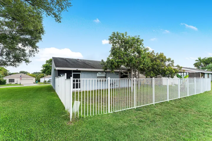Expansive green lawn bordering a white picket fence, surrounding a residence with a gray exterior and dark roof