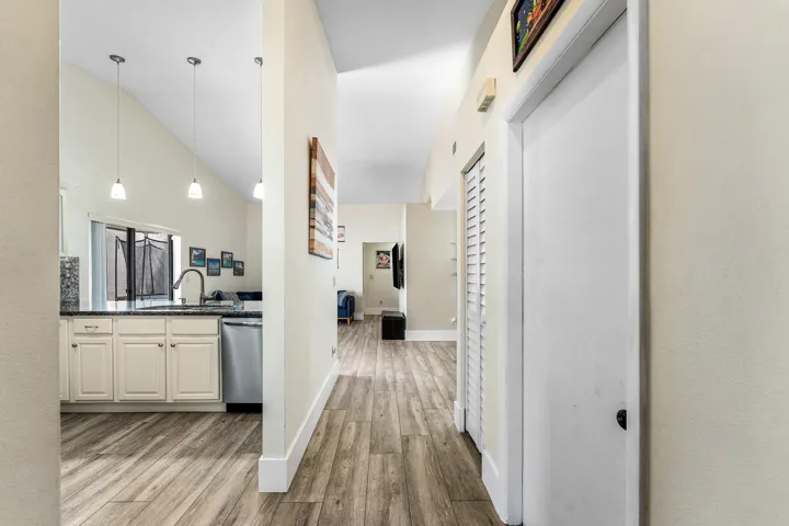 Hallway with wood-finish flooring extending into the kitchen, featuring light cream cabinetry, dark countertops, and stainless steel appliances