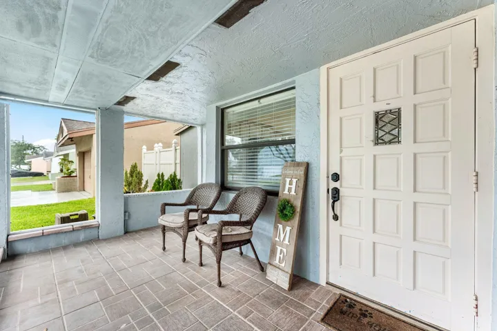 Covered front porch featuring a paneled entry door with decorative ironwork, tile flooring, and a large window with blinds