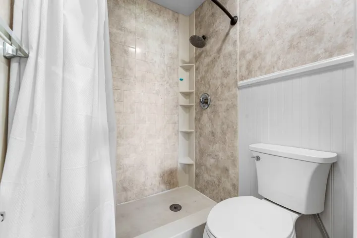 Tiled shower stall with a built-in shelf system, a black showerhead, and a chrome-finished mixer