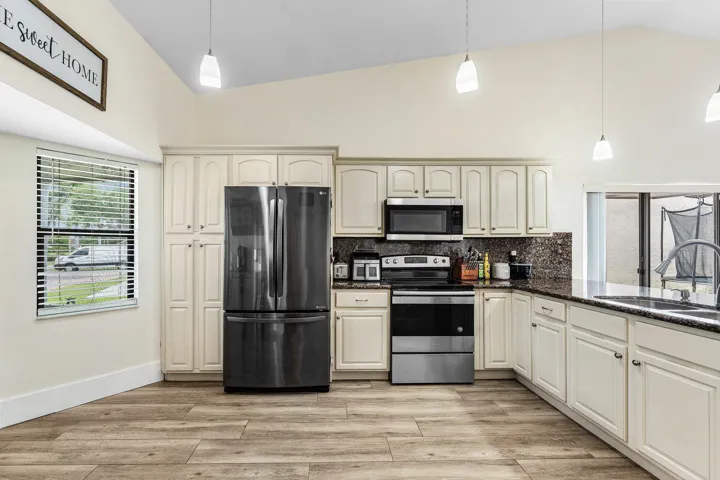 Kitchen featuring light-toned cabinetry, dark patterned countertops, stainless steel appliances, and wood-finish flooring