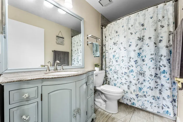 Bathroom featuring a light blue vanity with a curved front, a granite-look countertop, and a vanity mirror with overhead lighting