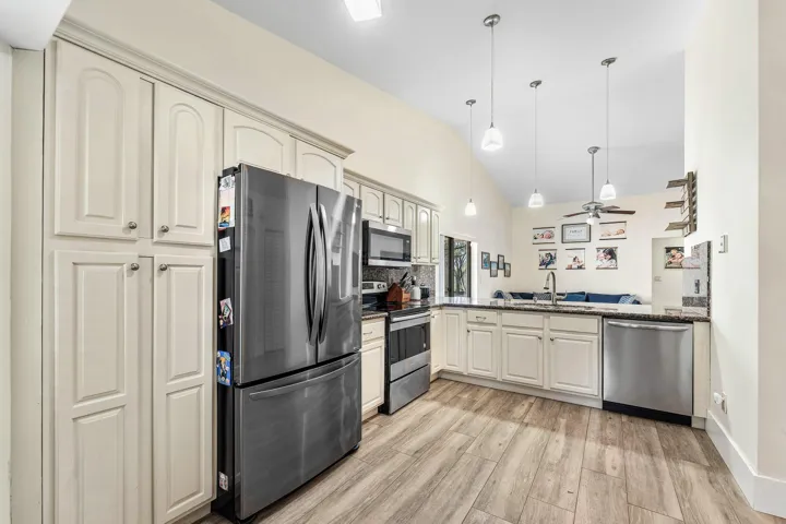 Kitchen featuring white cabinetry, stainless steel appliances, granite countertops, wood-finish flooring, and vaulted ceilings with pendant lighting