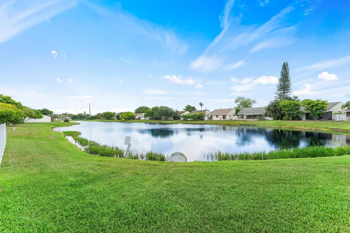 Expansive backyard featuring a large pond, lush green lawn, white perimeter fencing, and mature trees
