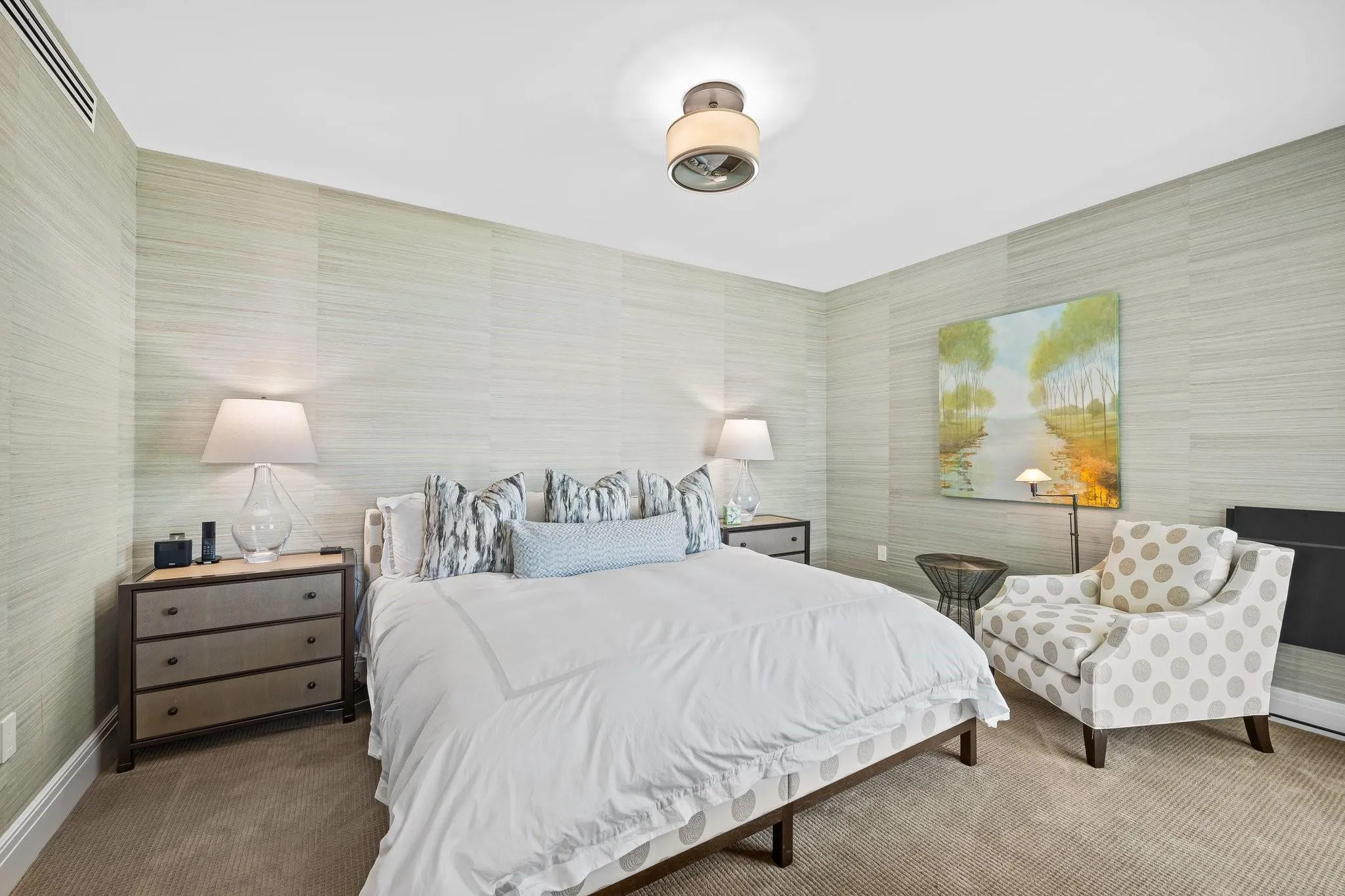 Bedroom featuring light-toned textured wall coverings, recessed air vent, and a ceiling-mounted light fixture