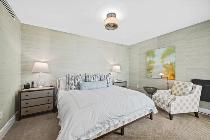 Bedroom featuring light-toned textured wall coverings, recessed air vent, and a ceiling-mounted light fixture