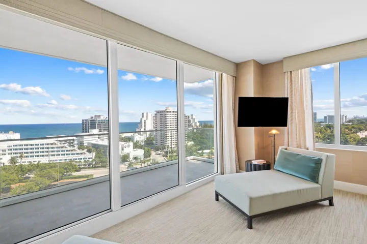Floor-to-ceiling glass doors opening onto an expansive balcony, featuring an ocean and city backdrop
