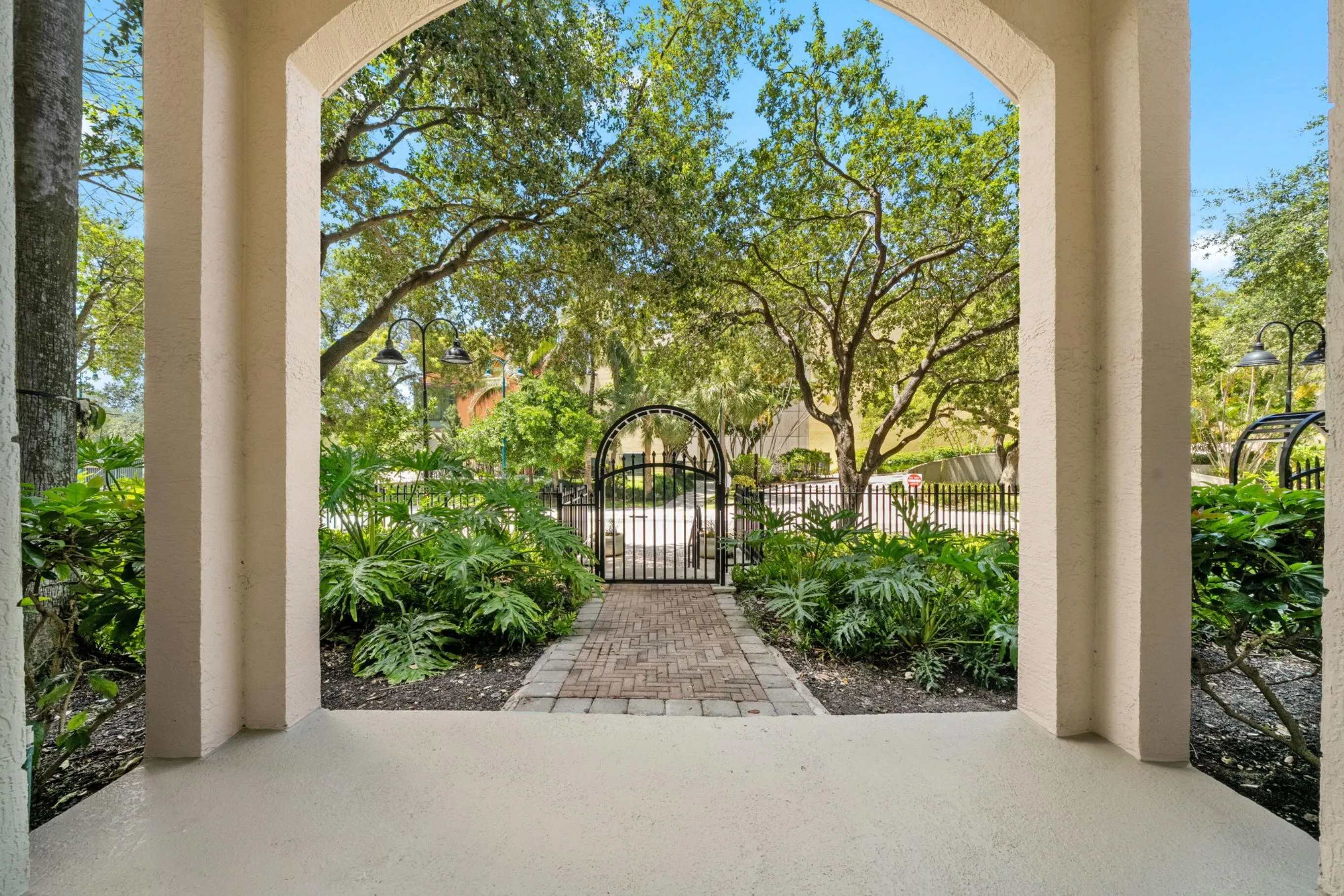 Covered private patio framed by lush landscaping, with a brick-paver path leading to the gated entrance on West Las Olas Boulevard.