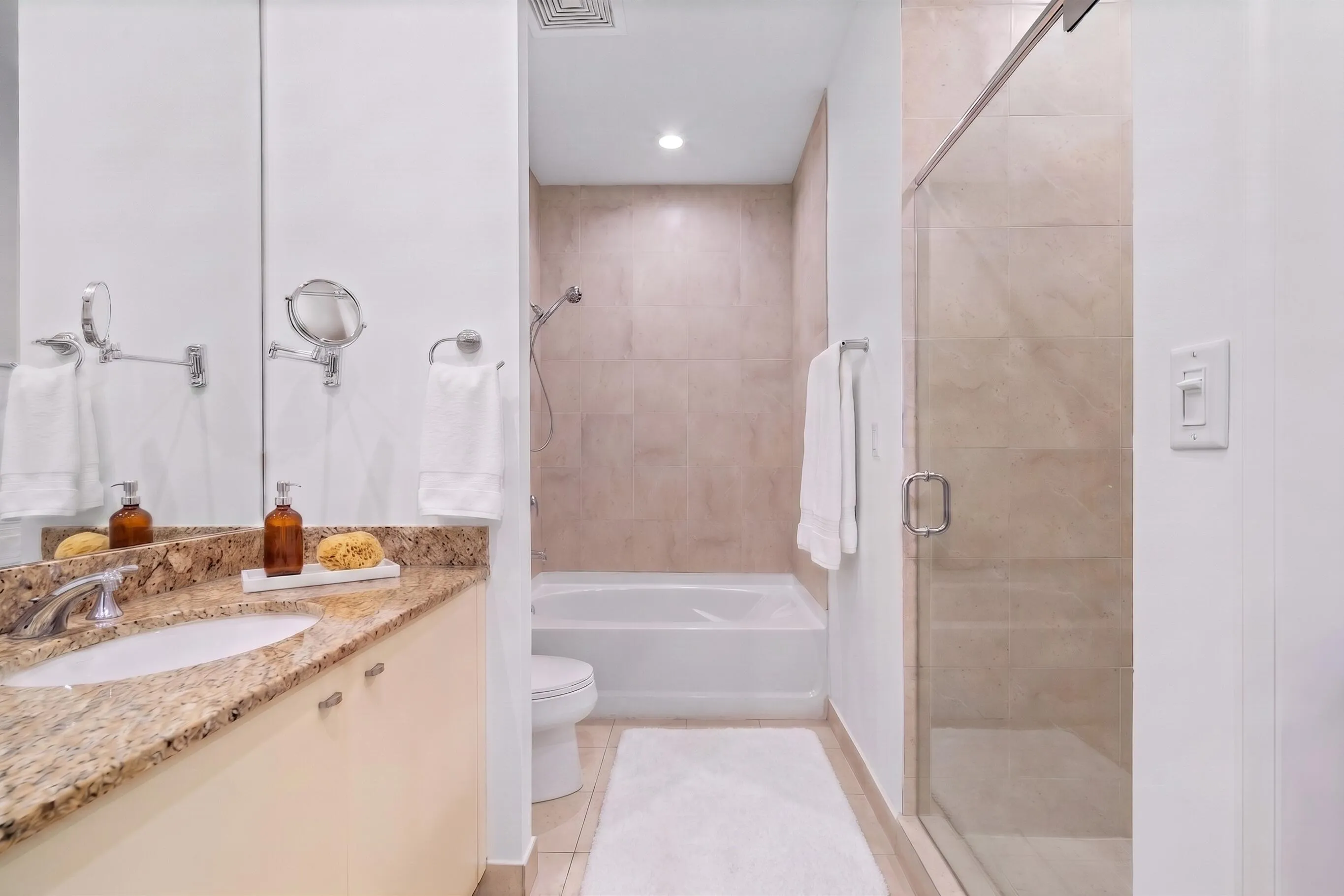 Spacious bathroom with a granite-topped vanity, large soaking tub & separate glass-enclosed walk-in shower with neutral tile finishes.