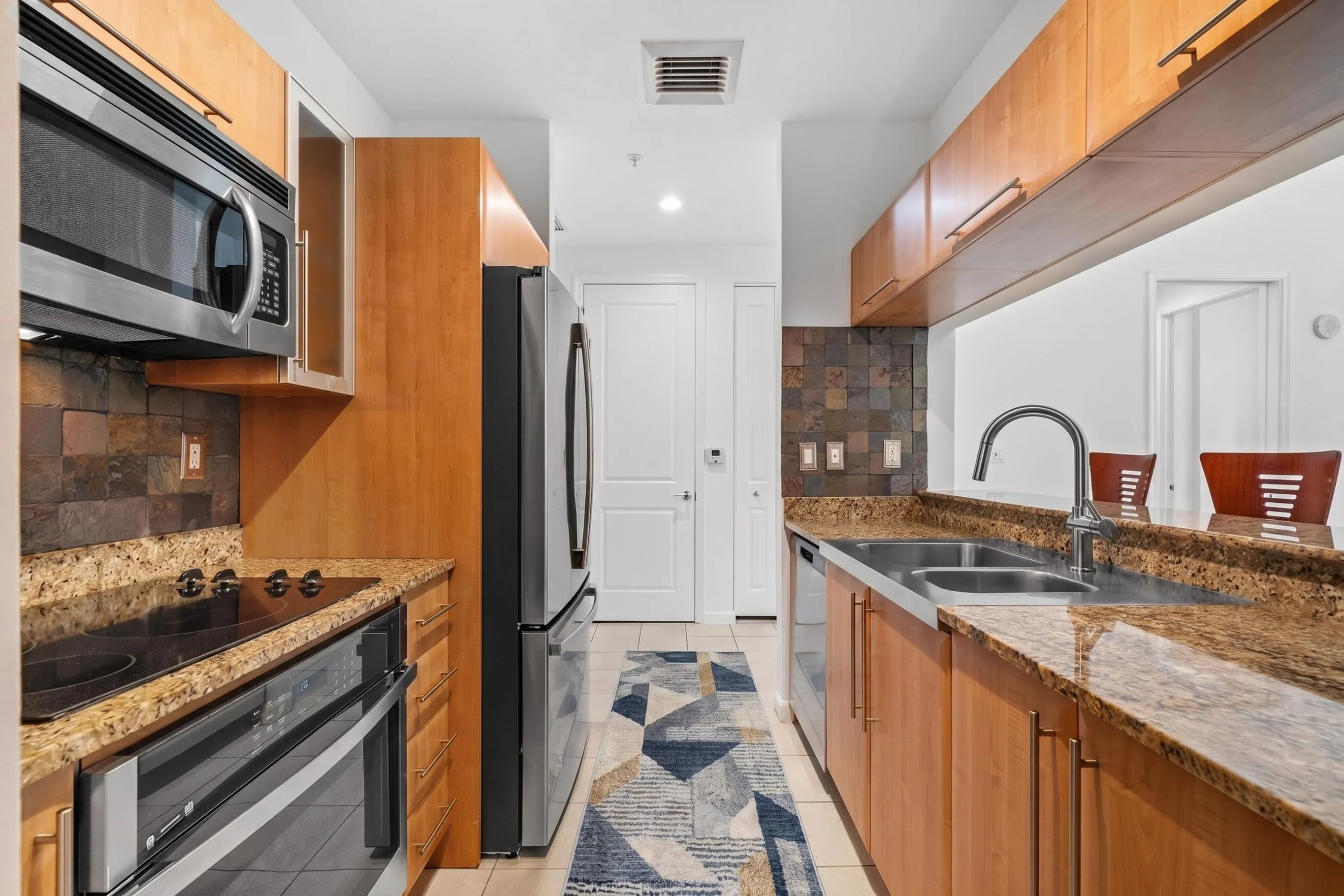 Alternate kitchen view featuring a glass electric cooktop, built-in oven & microwave, double-basin sink, pantry & breakfast-bar pass-through.