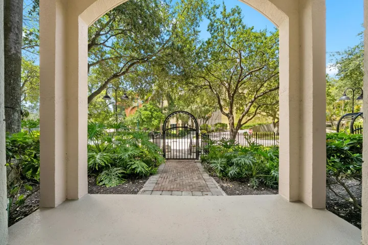 Covered private patio framed by lush landscaping, with a brick-paver path leading to the gated entrance on West Las Olas Boulevard.