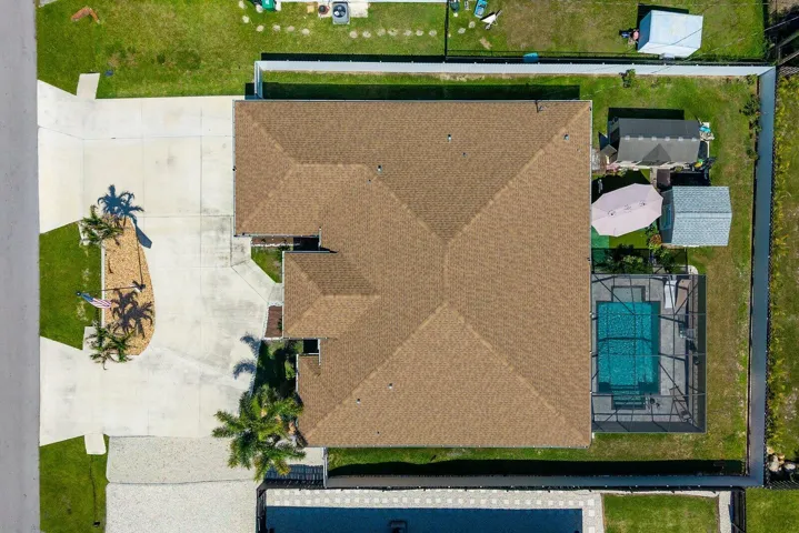 An elevated perspective showcases the screen-enclosed pool, covered lanai, fully fenced backyard, and two detached storage sheds, highlighting the thoughtful layout and generous outdoor living space.