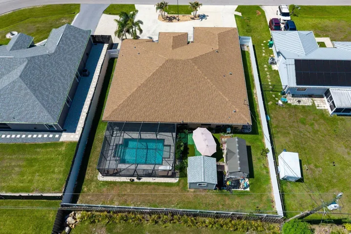 A bird's-eye view highlights the home's expansive footprint, circular driveway, screen-enclosed pool, fully fenced yard, and detached storage sheds, offering a unique perspective of the property's design and functionality.