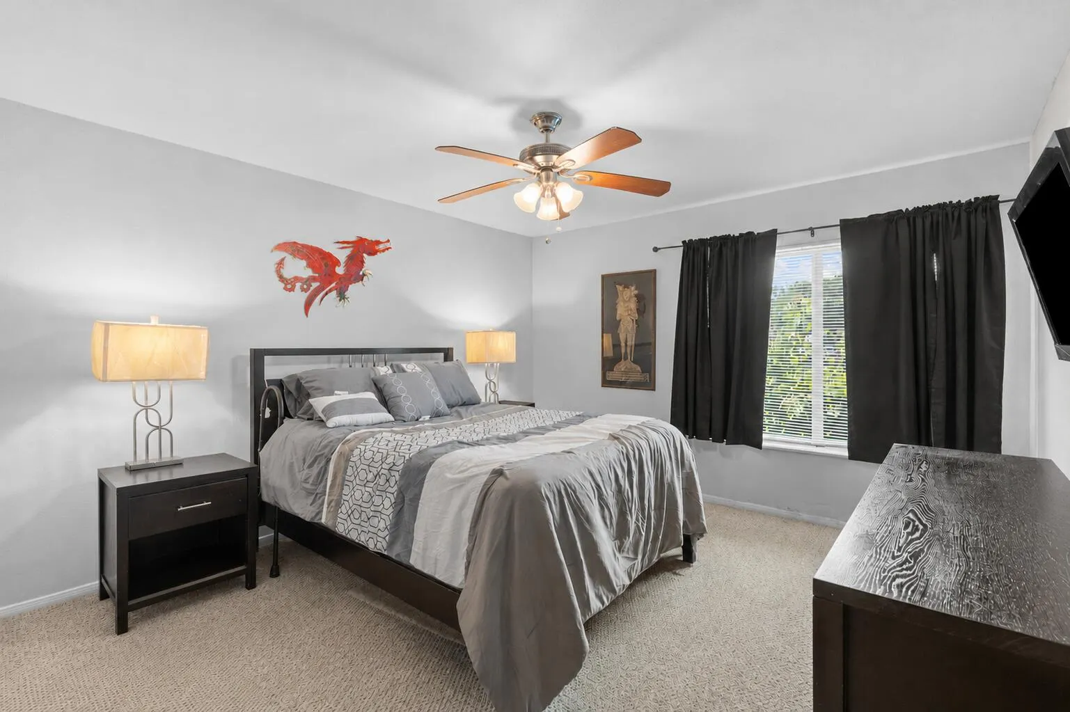 Spacious primary bedroom features neutral finishes, soft carpeting, a ceiling fan, and a large window that brings in natural light.
