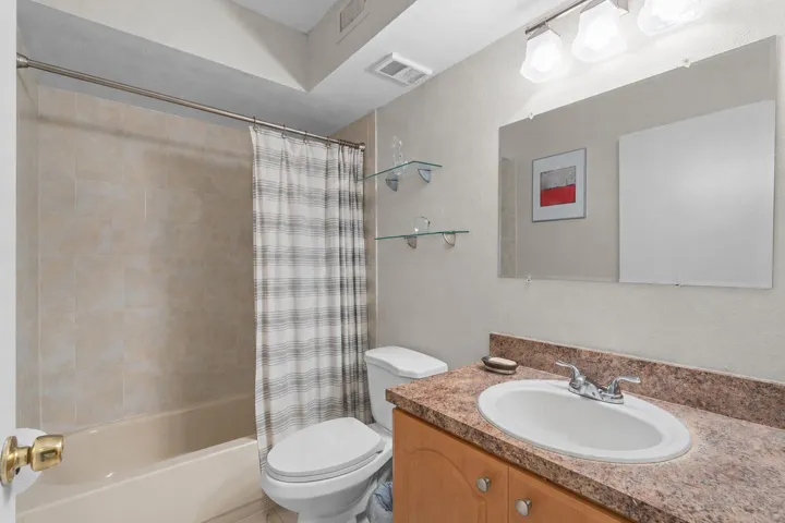 Hall bathroom with a single-sink vanity, tile surround tub and shower, and convenient built-in glass shelving.
