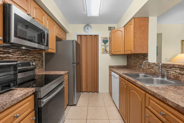 Galley-style kitchen equipped with stainless steel appliances, generous cabinetry, tile flooring, and a mosaic tile backsplash.