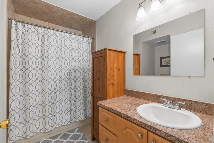 Private en-suite bath includes a single-sink vanity, tile tub and shower, and a linen cabinet for extra storage.