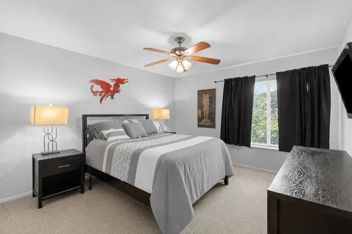 Spacious primary bedroom features neutral finishes, soft carpeting, a ceiling fan, and a large window that brings in natural light.