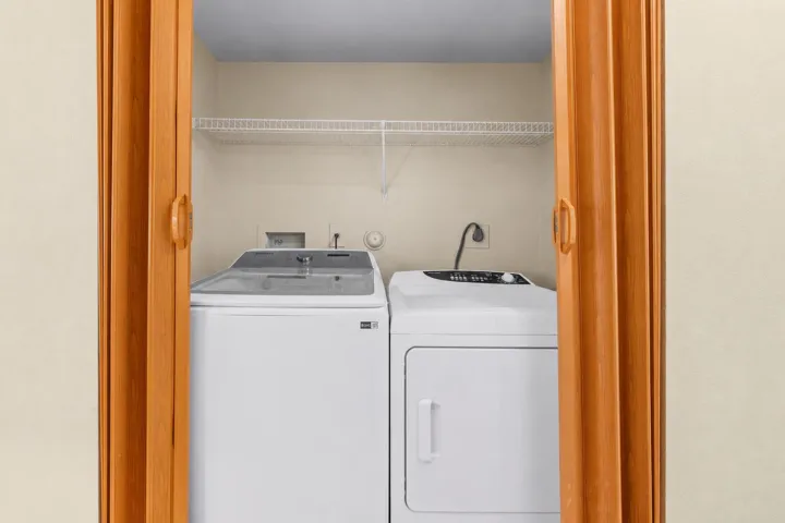 Dedicated laundry closet includes a side-by-side washer and dryer with overhead shelving for everyday storage.