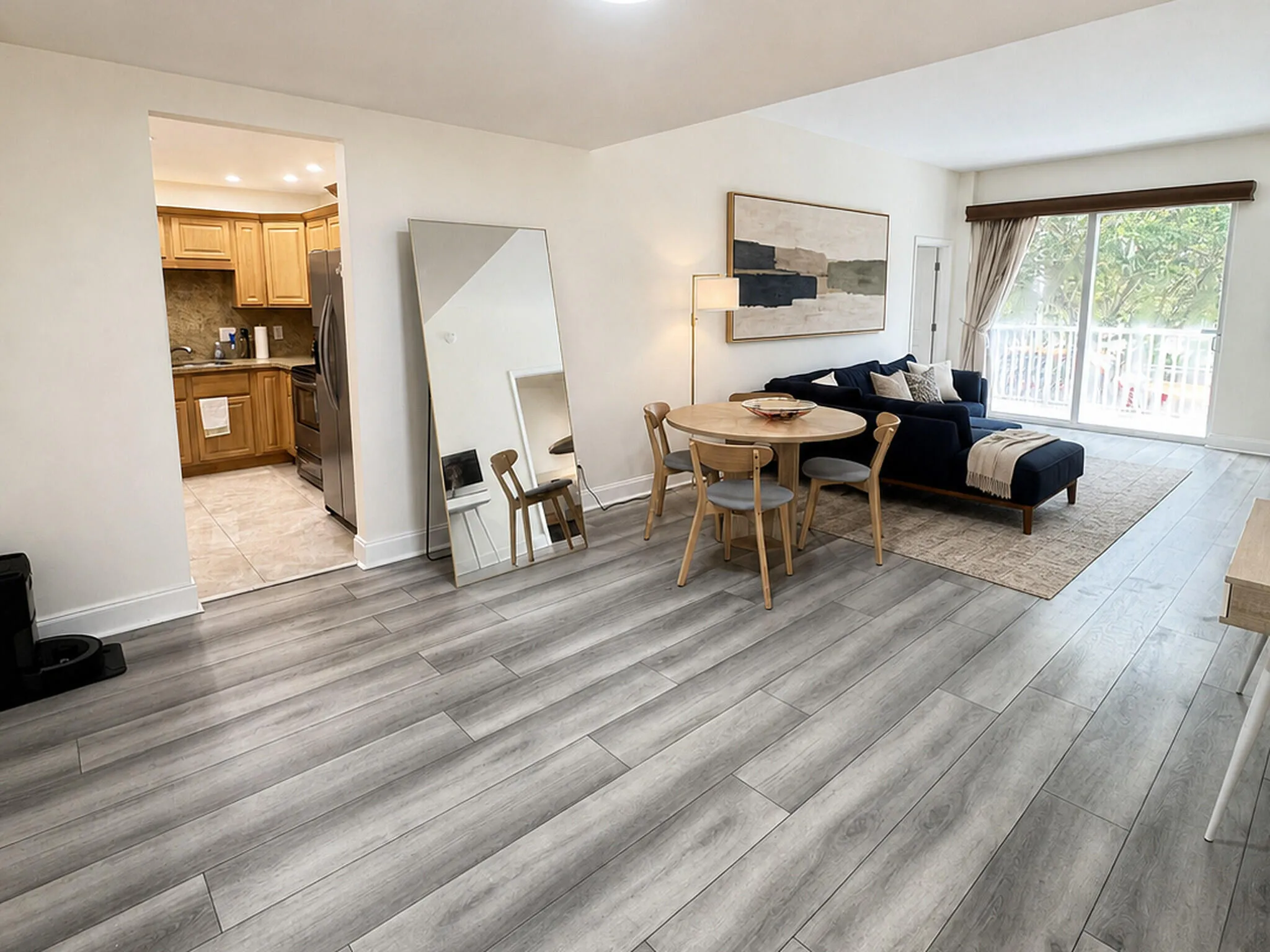 Spacious living area featuring light wood-finish flooring, white walls, and a sliding glass door with white railings