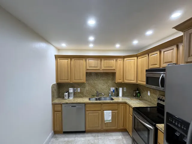 Kitchen featuring warm-toned wood cabinetry, stone countertops, and a full stone backsplash