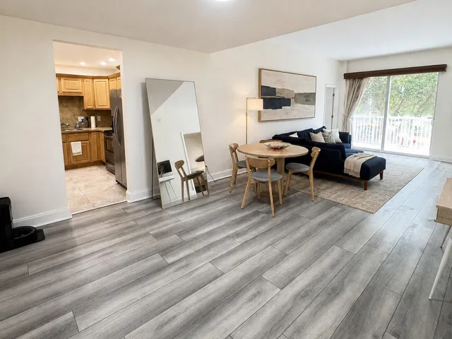 Spacious living area featuring light wood-finish flooring, white walls, and a sliding glass door with white railings