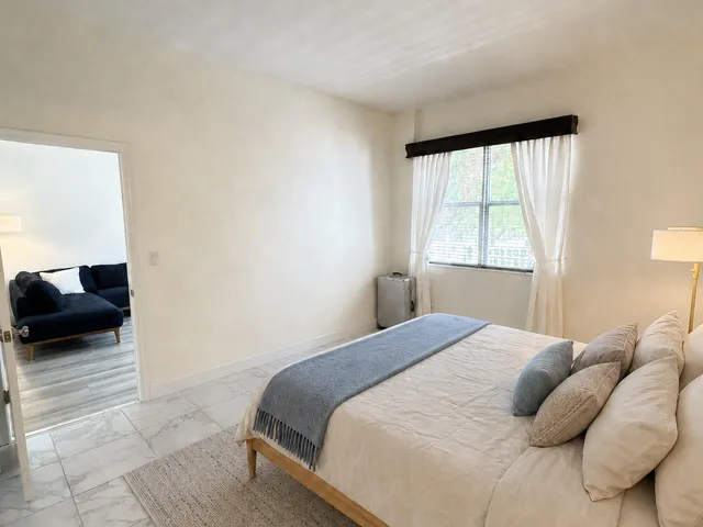 Bedroom featuring tile flooring, neutral wall tones, and a window with blinds and drapes