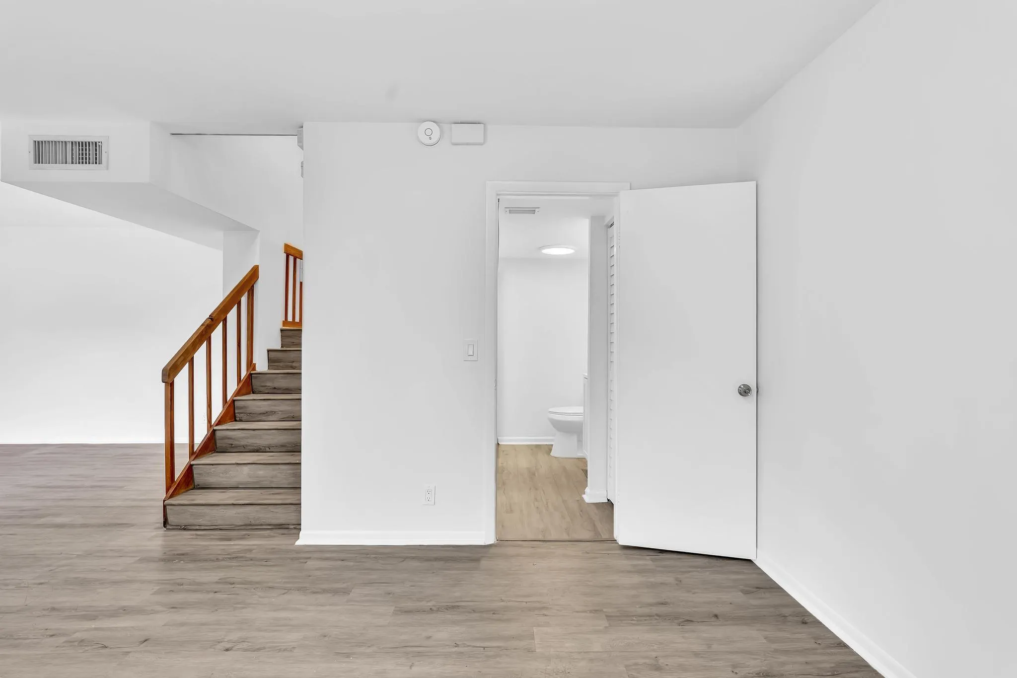 Spacious interior featuring wood-finish flooring, a staircase with wood railing, and white walls