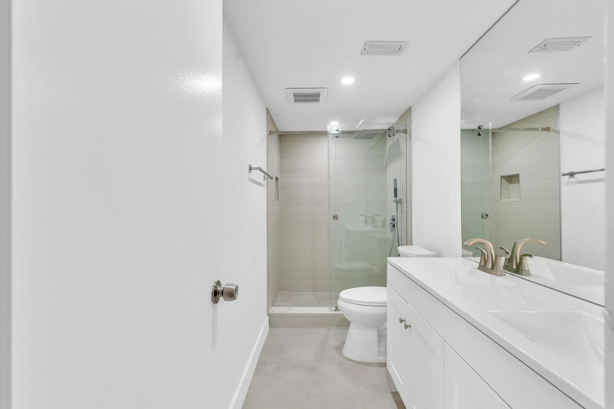 Contemporary bathroom featuring a spacious vanity with an integrated sink, a large wall-mounted mirror, and a glass-enclosed shower with a tiled niche